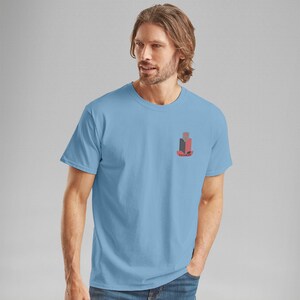K&ouml;nnte beinhalten: Hellblaues T-Shirt mit einem kleinen Aufdruck auf der Brust. Die Grafik zeigt ein stilisiertes Design in Rot und Schwarz mit dem Wort "FAIRWAY" darunter. Das T-Shirt hat einen klassischen Rundhalsausschnitt.