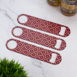 May include: Three stainless steel bottle openers with a red and black geometric pattern. The pattern resembles the carpet from the movie "The Shining".