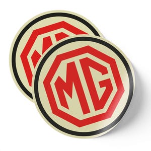 Puede incluir: Dos pegatinas redondas con el logotipo de MG. El logotipo es un hexágono rojo con las letras "MG" en su interior, sobre un fondo crema y delineado con un anillo negro.