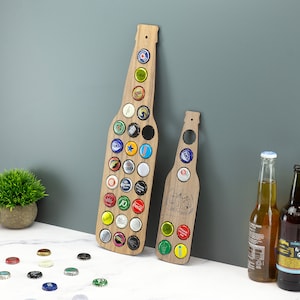 May include: Two wooden bottle cap holders shaped like beer bottles. The larger bottle has space for 28 bottle caps and the smaller bottle has space for 10 bottle caps. Both bottles have a brown wood finish.