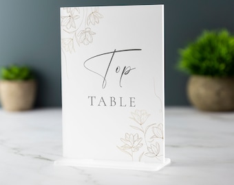 May include: White acrylic table number sign with gold floral design and the text "Top Table".