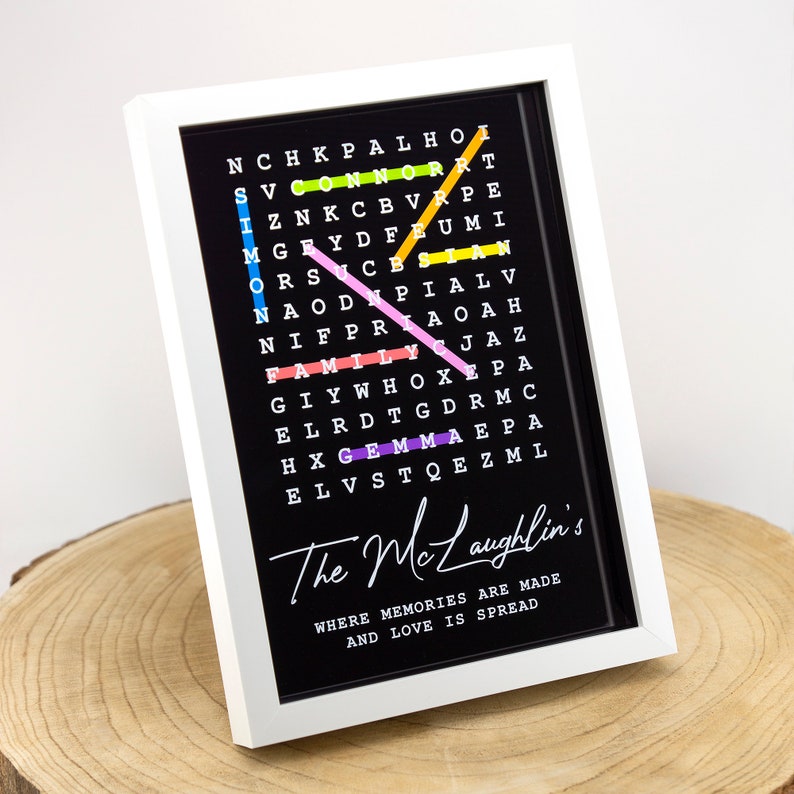 May include: A framed black and white word search puzzle with colorful letters spelling out the words "family", "love", "home", and "gem". The frame is white and the text below the puzzle reads "The McLaughlin's Where memories are made and love is spread".