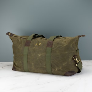 May include: A green canvas duffel bag with brown leather accents and green straps. The bag has a zipper closure and a personalised monogram that reads "A.Z."