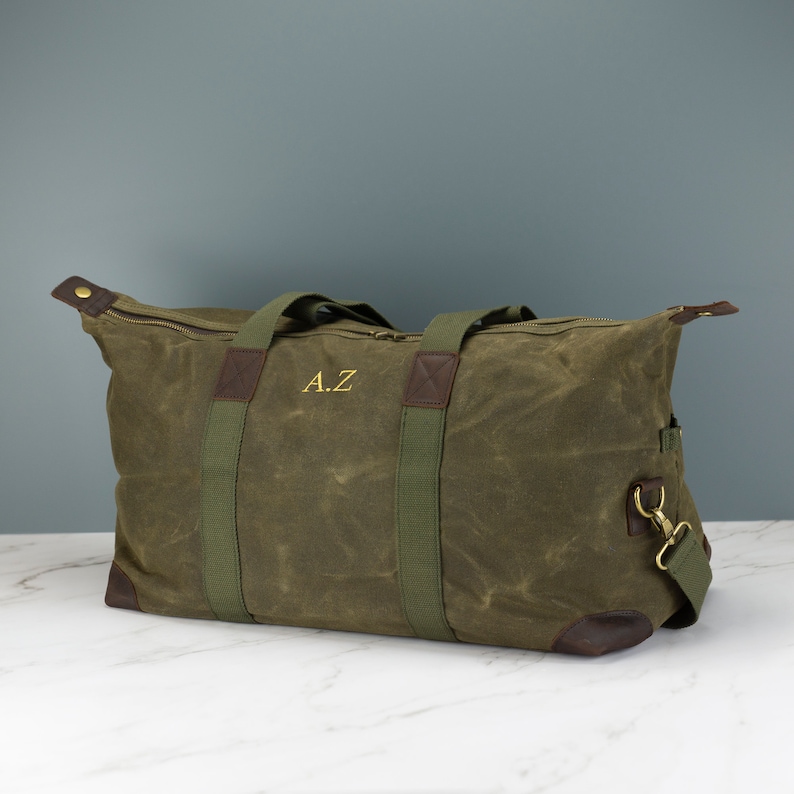 May include: A green canvas duffel bag with brown leather accents and green straps. The bag has a zipper closure and a personalised monogram that reads "A.Z."