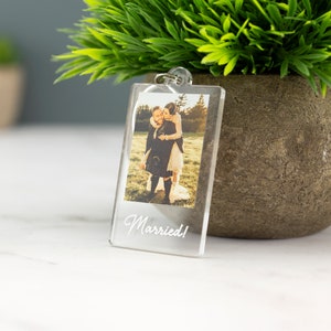May include: A clear acrylic keychain with a photo of a couple in a field. The text "Married!" is printed on the keychain.