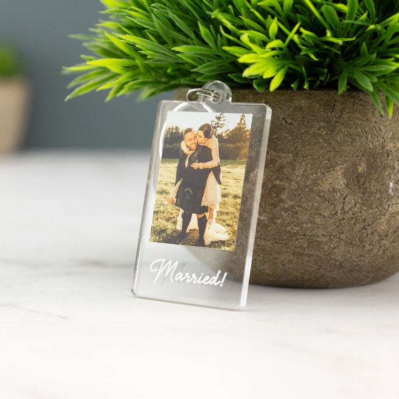 May include: A clear acrylic keychain with a photo of a couple in a field. The text "Married!" is printed on the keychain.