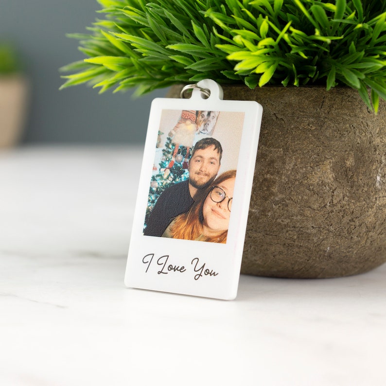 May include: White photo keychain with a picture of a couple in front of a Christmas tree. The text "I Love You" is printed below the photo.