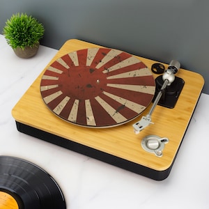 May include: A bamboo turntable with a red and white sunburst design on the record player. The turntable has a silver tone arm and controls. A black vinyl record is visible in the foreground.