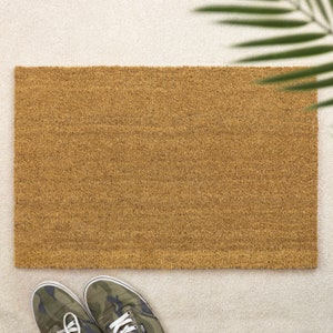 May include: A brown coir doormat with a textured surface. The doormat is on a white surface.