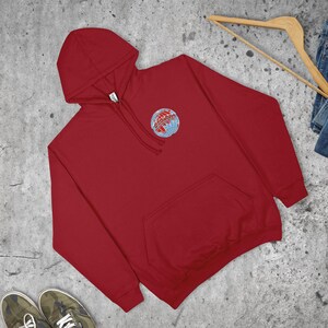 May include: A crimson hooded sweatshirt with a kangaroo pocket and a small embroidered globe design on the chest. The design includes the word "Adventures".