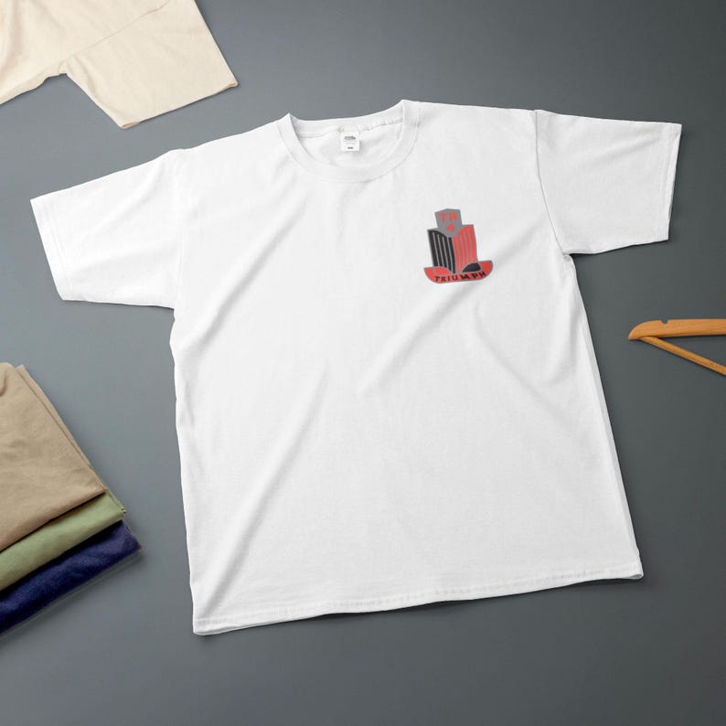 K&ouml;nnte beinhalten: Wei&szlig;es T-Shirt mit einer kleinen Grafik auf der Brust. Die Grafik zeigt ein stilisiertes Design in Rot, Schwarz und Grau mit dem Wort "TRIUMPH" in Rot. Zus&auml;tzliche gefaltete Hemden sind im Bild zu sehen.