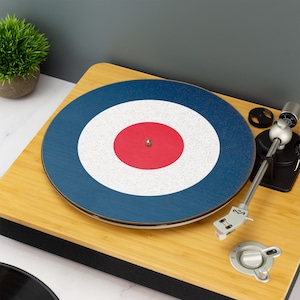 以下が含まれることがあります： 赤色の円の中心に、青と白のターゲット模様のレコードプレーヤーの滑り止めマット。滑り止めマットは木製のターンテーブルの上に置かれています。