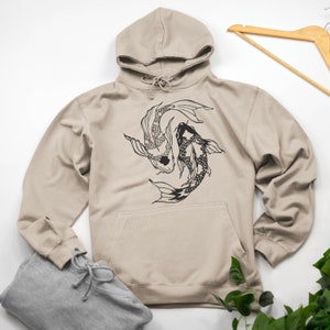 Może przedstawiać: Beżowa bluza z kapturem z czarno-białym nadrukiem dwóch karpi koi pływających w kółko. Bluza ma kaptur ze sznurkiem i kieszeń kangurkę.