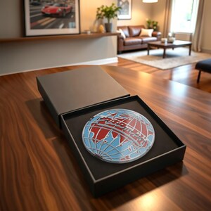 May include: A round, red, white, and blue globe design is displayed inside a black box. The globe features a detailed map with continents and oceans. The box is open, revealing the globe against a black interior.