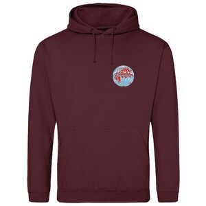 May include: A burgundy-coloured hoodie with a front pocket and a hood with drawstrings. It has a small, circular emblem on the upper left chest. The emblem is a globe design with red, white, and blue accents.