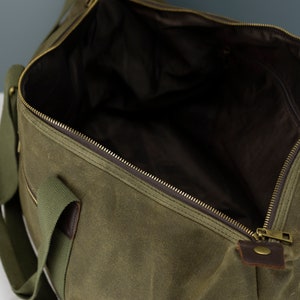 May include: An olive green canvas duffel bag with a zipper closure and a brown leather accent. The bag has a single strap and two handles.