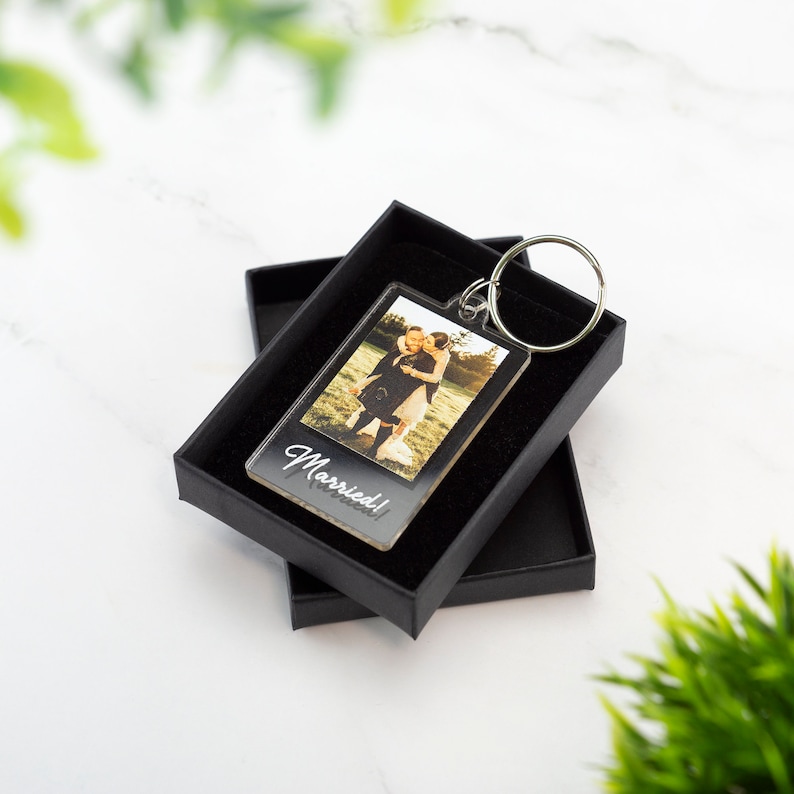 May include: A clear acrylic keychain with a photo of a couple in a field. The keychain has a silver ring and the text "Married!" printed on the bottom.