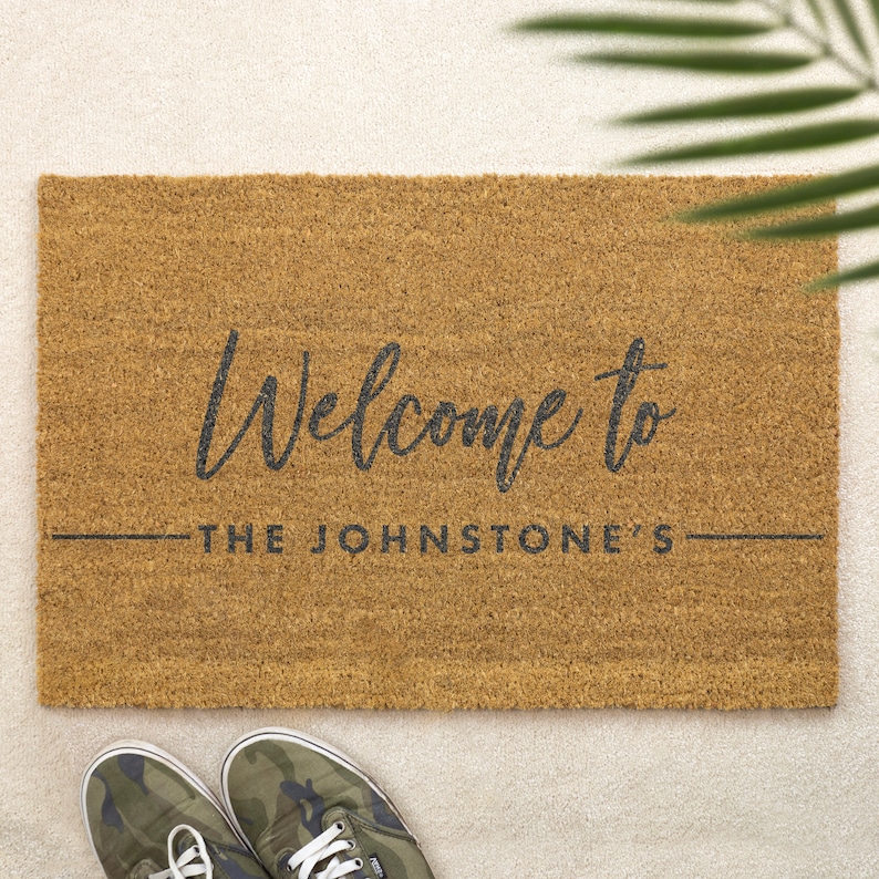 May include: A brown coir doormat with the text "Welcome to The Johnstone's" in black lettering.