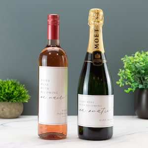 May include: Two bottles of wine with personalized labels. The label on the rose wine bottle reads "Pairs well with becoming an uncle" and the label on the champagne bottle reads "Pairs well with becoming an auntie".