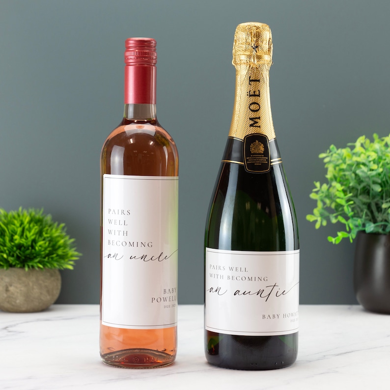 May include: Two bottles of wine with personalized labels. The label on the rose wine bottle reads "Pairs well with becoming an uncle" and the label on the champagne bottle reads "Pairs well with becoming an auntie".