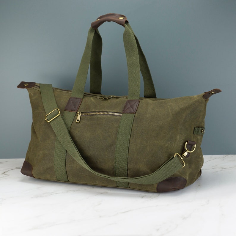 May include: A green canvas duffel bag with brown leather accents and a zipped pocket. The bag has a top handle and a detachable shoulder strap.