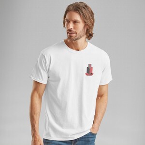 K&ouml;nnte beinhalten: Wei&szlig;es T-Shirt mit einem kleinen, stilisierten Geb&auml;ude-Grafik in Rot, Schwarz und Grau auf der linken Brust. Das Wort "FAIRWAY" steht darunter. Das T-Shirt hat kurze &Auml;rmel.