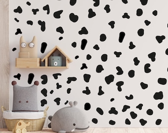 May include: A white wall with black irregular shaped spots, resembling a dalmatian dog pattern. The wall is decorated with black and white wall decals. There are stuffed animals and a toy car on a shelf in front of the wall.