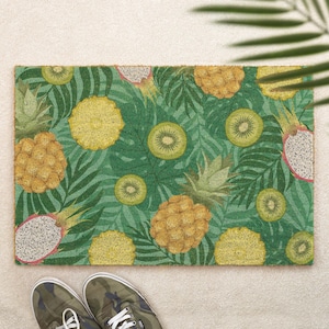 May include: A rectangular doormat featuring a vibrant tropical pattern of yellow pineapples, sliced green kiwi fruit, and pink dragon fruit set against a background of dark green palm leaves and foliage, creating a dense, colourful botanical design.