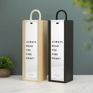 Puede incluir: Dos cajas de regalo de madera para botellas de vino con asas de cuerda. Las cajas son de madera natural y negra. Ambas cajas tienen una etiqueta blanca con el texto "Always Read The Fine Print."