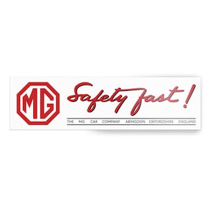 Op de afbeelding: Een rechthoekige witte sticker met het rode MG-logo en de tekst "Safety Fast!" in rode letters. Daaronder staat in zwarte tekst "THE MG CAR COMPANY ABINGDON OXFORDSHIRE ENGLAND".