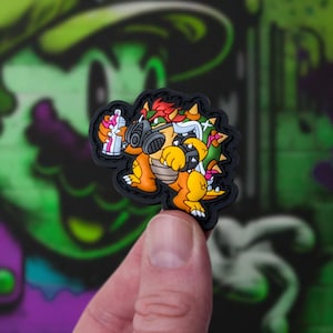 Op de afbeelding: Een zwart en geel cartoonfiguur met een gasmasker en een spuitbus. Het personage is een populair videogamepersonage.