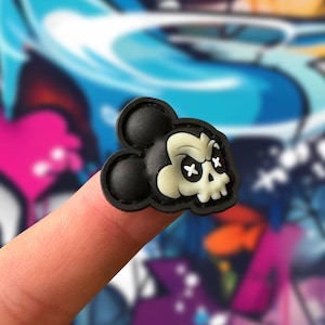 Puede incluir: Encanto de personaje de Mickey Mouse con forma de calavera en blanco y negro con una expresión amenazante. El encanto está hecho de goma y tiene un efecto 3D.