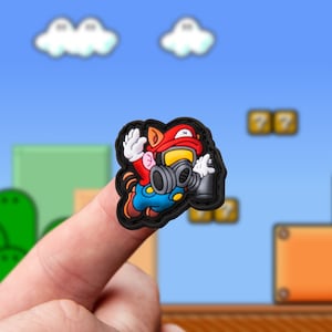 May include: A red and black 3D character wearing a gas mask and holding a spray can. The character is in a jumping pose with a red hat and blue overalls. The character is on a finger in front of a video game background.