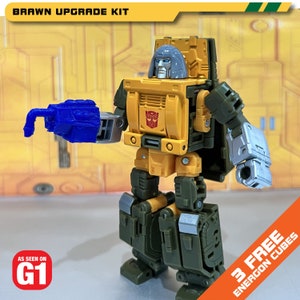 May include: A yellow and green robot toy with a blue hand, a gray helmet, and the text "BRAWN UPGRADE KIT" and "AS SEEN ON G1" on the image. The robot is standing on a yellow and brown background. The text "3 FREE ENERCON CUBES" is on the bottom right corner of the image.