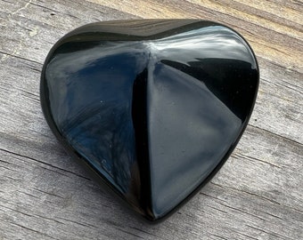 May include: A black obsidian heart-shaped crystal. The crystal is polished and has a smooth, shiny surface.