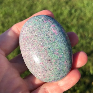 May include: A smooth, oval-shaped green and pink gemstone with a speckled pattern.