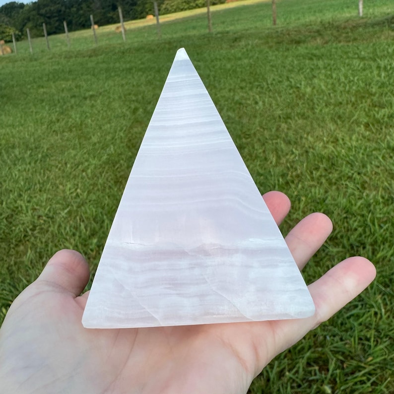 Op de afbeelding: Een witte seleniet piramidekristal met een glad, gepolijst oppervlak. De piramide is ongeveer 15 cm hoog en heeft een driehoekige basis.