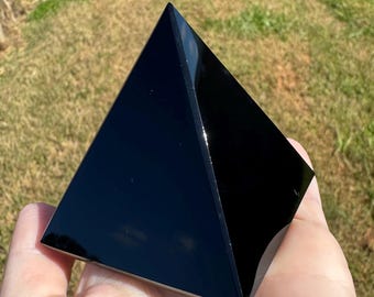 Op de afbeelding: Een gladde, gepolijste zwarte piramide met een reflecterend oppervlak. Het object heeft vier driehoekige zijden die samenkomen in een scherpe top, met een diepe, effen zwarte kleur en subtiele lichtreflecties op de glanzende buitenkant.