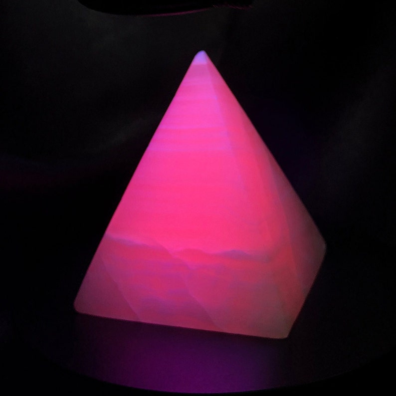 Op de afbeelding: Een roze piramidevormig kristal met witte strepen. Het kristal gloeit onder een zwarte lamp.
