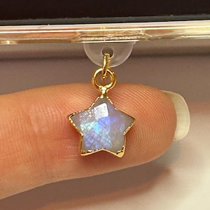 Puede incluir: Un charm en forma de estrella dorada con una piedra iridiscente facetada en el centro. El charm está suspendido de un pequeño lazo de plástico transparente. La palabra "kindle" es visible en el fondo.