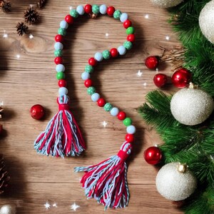 May include: A Christmas garland made of red, white, and green beads with a white and red tassel on each end.