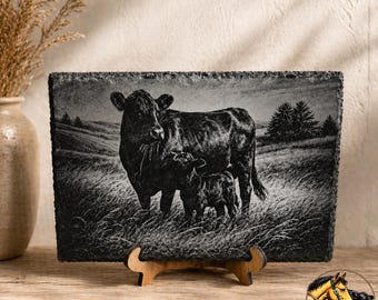 May include: A black and white slate plaque featuring a cow and calf in a grassy field. The rectangular plaque is displayed on a wooden stand. The image has a rustic, country theme. The Dun & Dust Co. logo is visible in the lower right corner.