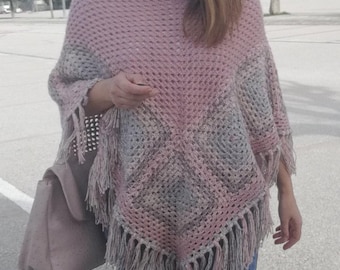Puede incluir: Un poncho de crochet rosa y gris con flecos. El poncho está hecho de un hilo ligero y tiene un corte holgado.