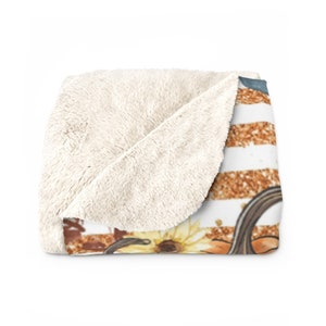 May include: A soft, white fleece throw blanket with a printed design of pumpkins, sunflowers, and gold glitter stripes on the front side.