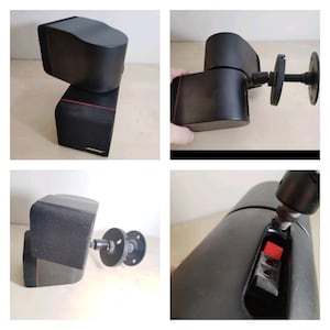 May include: Black Bose speakers with a red accent line. The speakers have a rectangular shape with a mesh front and a curved top. One speaker is mounted on a wall bracket. The Bose logo is visible on the front of one speaker.