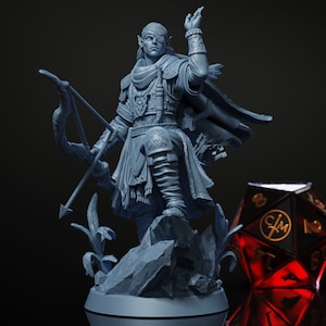May include: A gray painted miniature figurine of an elf archer with a bow and arrow, standing on a rocky base with green plants. The elf is wearing a leather jerkin, a cloak, and a blindfold over one eye.