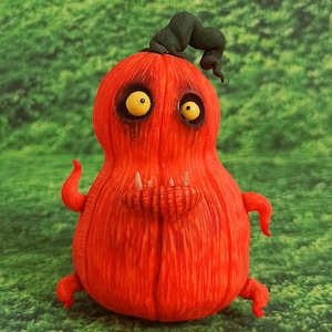 Puede incluir: Una calabaza roja texturizada con un tallo verde y dos ojos amarillos. La calabaza tiene una amplia sonrisa con dientes y parece ser una decoración de Halloween.
