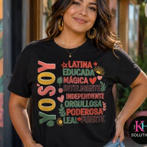 May include: A black short-sleeve t-shirt featuring the vertical text YO SOY and a list of words including LATINA, EDUCADA, MÁGICA, INTELIGENTE, INDEPENDIENTE, ORGULLOSA, PODEROSA, LEAL, and FUERTE, accented with small colorful icons like hearts and flowers.