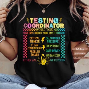 May include: Black t-shirt with the words "Testing Coordinator" in colorful text. The shirt lists qualities like "Critical Thinker" and "Supportive." The phrase "Some days I rock it, some days it rocks me" is also printed on the shirt.