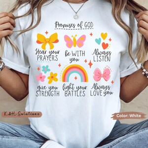 May include: White t-shirt with colorful graphics and text. The design includes a rainbow, butterflies, bows, hearts, and flowers, along with the words "Promises of GOD". The shirt is a casual wear item.